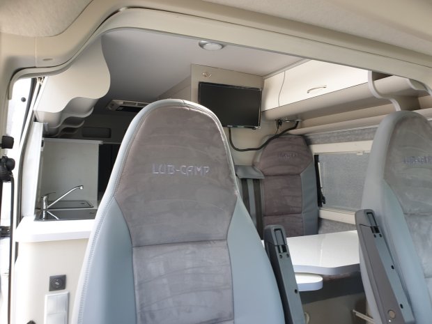 Wnętrze kampera z dwoma fotelami LUB-CAMP, aneksem kuchennym, stołem i telewizorem.