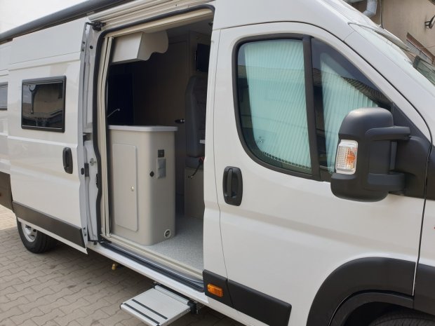 Biały kamper z otwartymi drzwiami bocznymi i wysuwanym stopniem.