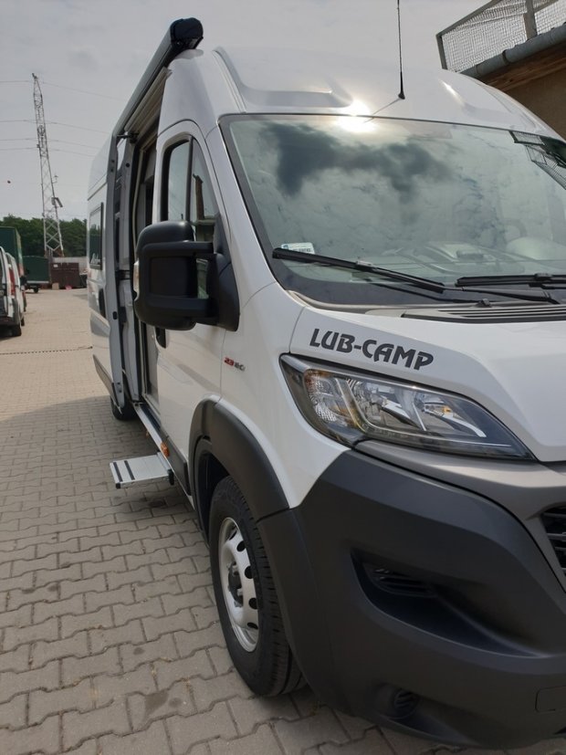 Biały kamper LUB-CAMP, przedni prawy bok z otwartymi drzwiami i wysuniętym stopniem