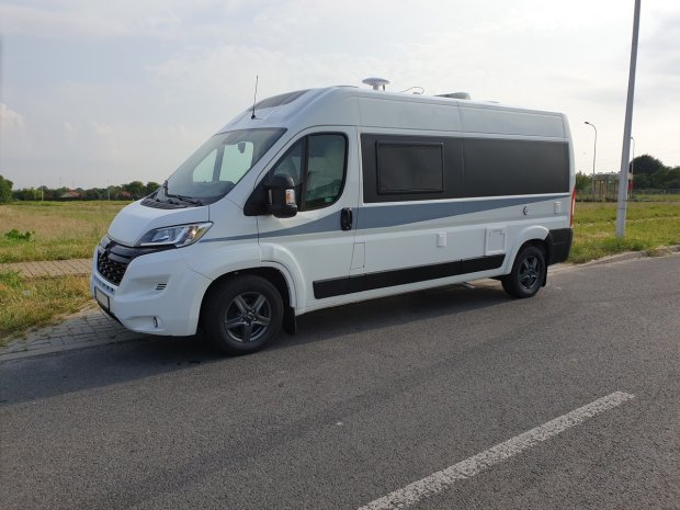 Biały kamper van zaparkowany przy drodze na tle pól.