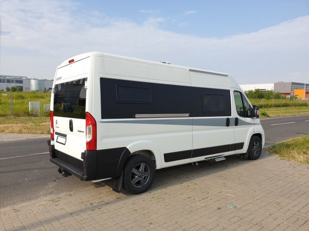 Biały kamper van z czarnymi panelami zaparkowany przy chodniku i drodze