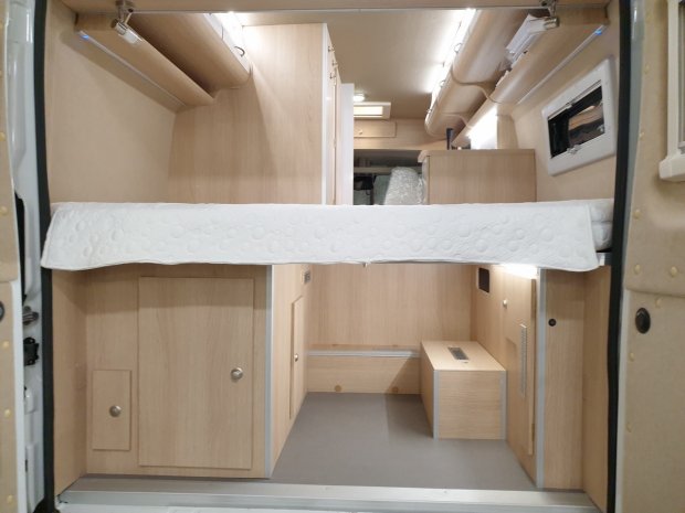 Wnętrze kampera z drewnianymi szafkami i piętrowym łóżkiem.