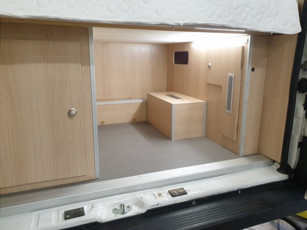 Schowek pod łóżkiem kampera z jasną drewnianą zabudową i skrzynką