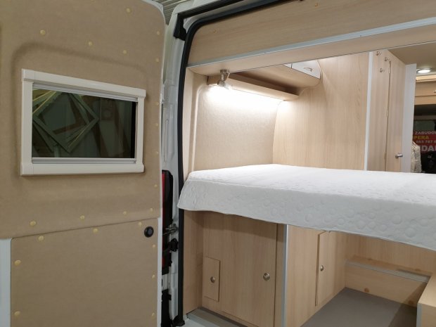 Wnętrze kampera z łóżkiem, jasnym drewnem i małym oknem