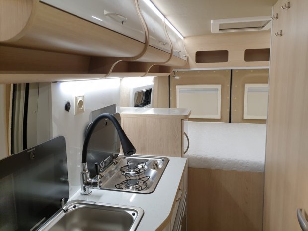 Wnętrze kampera: aneks kuchenny ze zlewem, kuchenką i łóżkiem z tyłu.