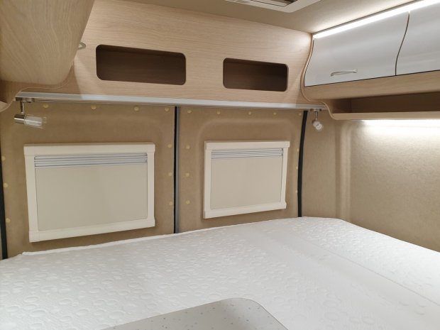 Wnętrze przytulnej kabiny z łóżkiem, zamkniętymi okienkami i górnymi szafkami.