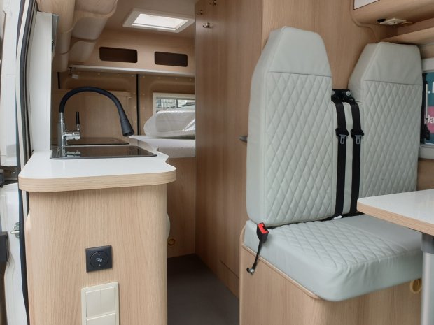 Wnętrze kampera z jasnymi pikowanymi fotelami, kuchenką i zlewem