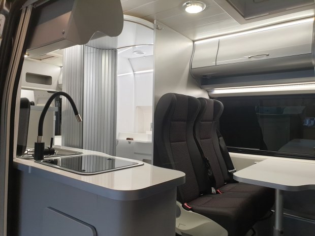 Wnętrze kampera z aneksem kuchennym, zlewem, dwoma fotelami i stolikiem