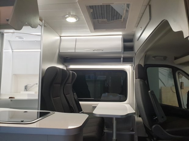 Wnętrze kampera z siedzeniami, stołem, szafkami i oknem