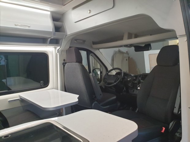 Wnętrze kampera z przednimi fotelami, stołem i panelem kierowcy.