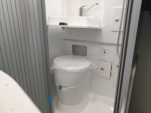 Mała łazienka kempingowa: toaleta z plastikowym siedzeniem, umywalka i prysznic
