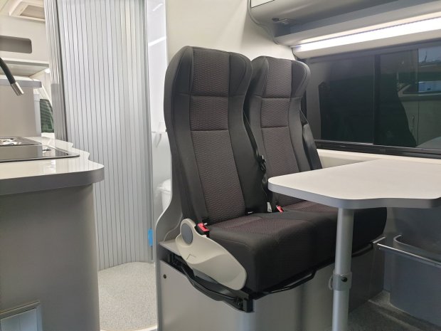 Dwa czarne fotele obok stolika we wnętrzu kampera