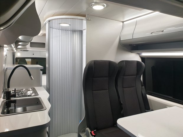 Wnętrze kampera: kuchnia z kranem i zlewem oraz dwa fotele przy stoliku.