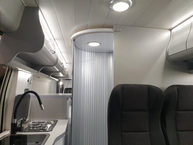 Wnętrze kampera z kuchnią, zlewem, kuchenką i przesuwną kabiną prysznicową