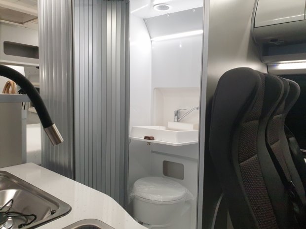 Wnętrze kampera: łazienka z umywalką i toaletą obok kuchennego blatu i kranu