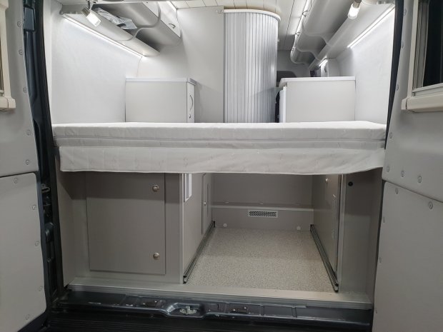 Wnętrze kampera: podwyższone łóżko nad schowkami i szafkami