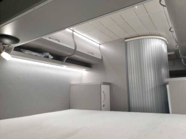 Wnętrze kampera: łóżko, półki bagażowe, oświetlenie LED i zaokrąglone drzwi przesuwne