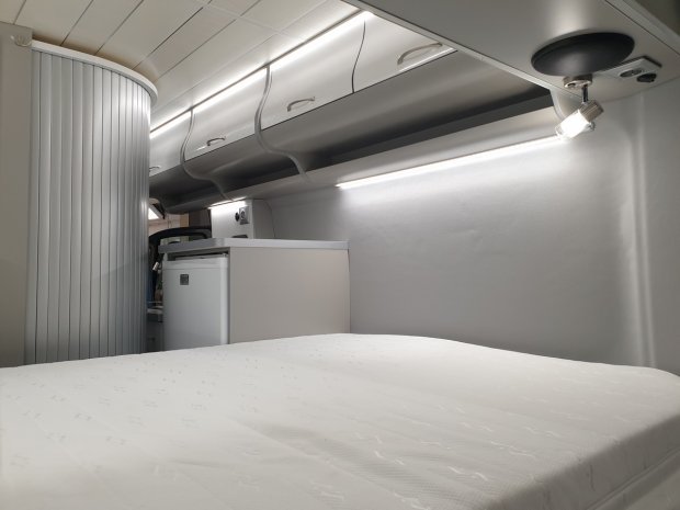 Wnętrze kampera: łóżko, szafki nad głową, mini-lodówka i oświetlenie LED
