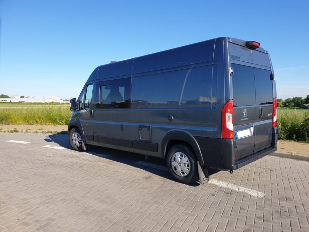 Ciemnoszary kamper-peugeot zaparkowany z boku na parkingu przy polu