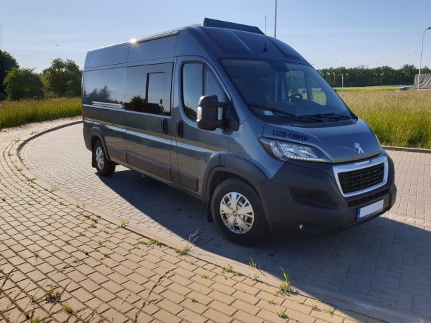 Szary camper van Peugeot LUB‑CAMP zaparkowany na brukowanym zakręcie w słoneczny dzień