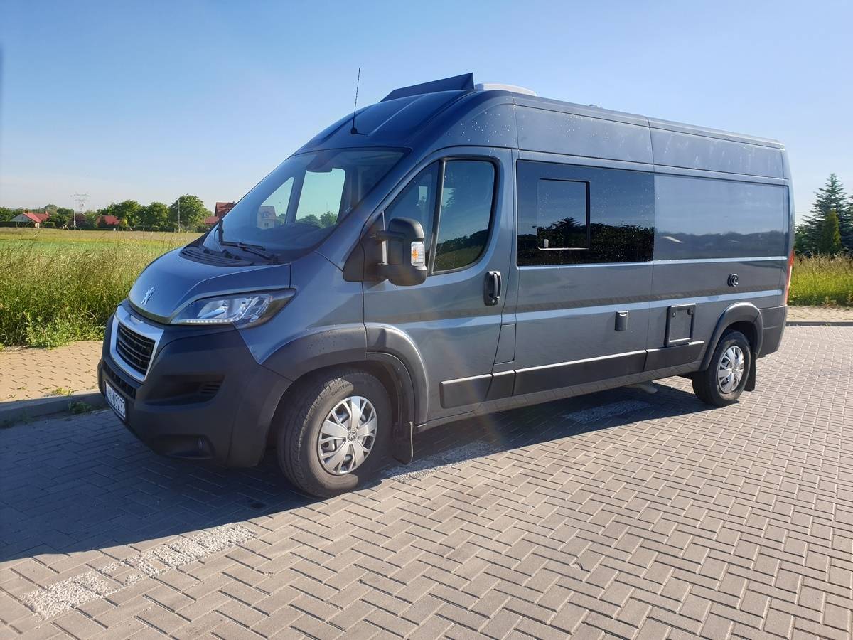 Szary van kamper zaparkowany na brukowanym placu obok pola