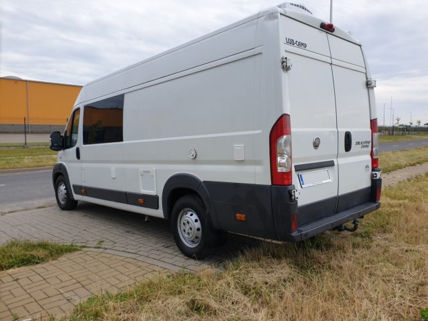 Biały kamper Fiat Ducato zaparkowany na chodniku w przydrożnym terenie