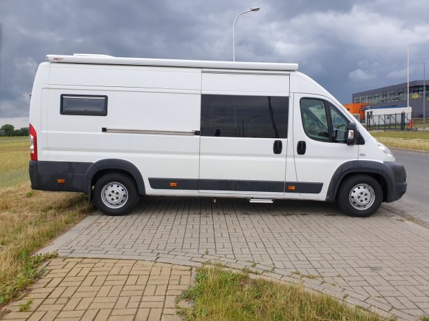 Biały kamper zaparkowany na chodniku pod burzowym, ciemnym niebem.