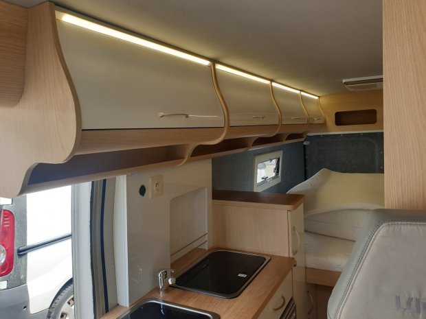 Wnętrze kampera: aneks kuchenny, górne szafki z oświetleniem i łóżko