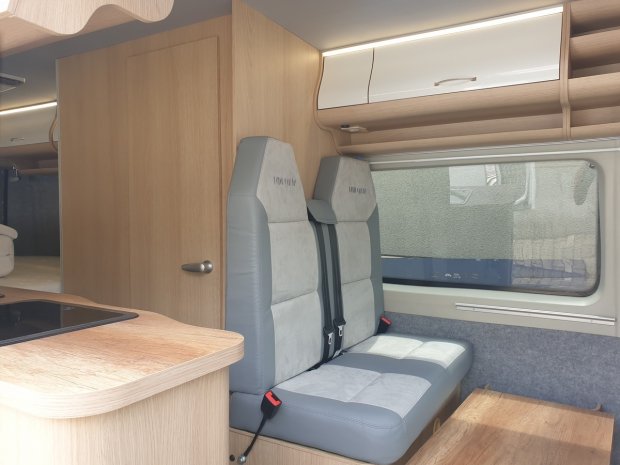 Wnętrze kampera z dwoma szarymi fotelami i drewnianymi szafkami przy oknie