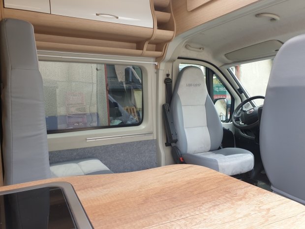 Wnętrze kampera: stół, obrócone fotele kierowcy i pasażera oraz półki nad oknem