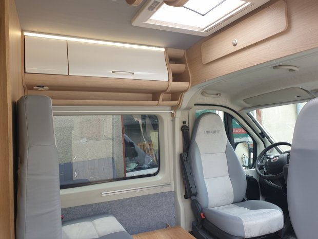 Wnętrze kampera z szarymi fotelami, drewnianymi szafkami i oknem dachowym