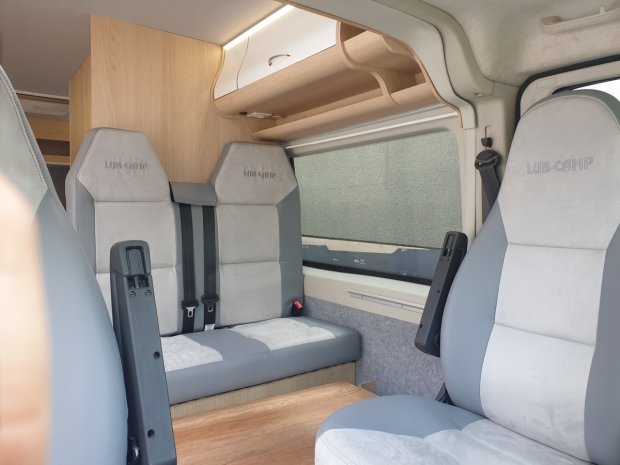 Wnętrze kampera: szare fotele, kanapa i drewniane półki