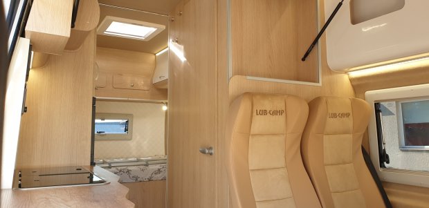 Wnętrze kampera z jasnym drewnem, kuchenką i dwoma beżowymi fotelami LUB‑CAMP