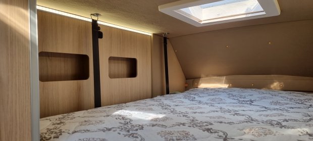 Łóżko w kamperze z ozdobnym materacem, drewniane panele i świetlik sufitowy