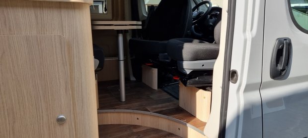Wnętrze kampera: otwarte drzwi, obrócony fotel kierowcy i drewniana zabudowa