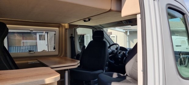 Wnętrze kampera z fotelem kierowcy, stołem i bocznym oknem