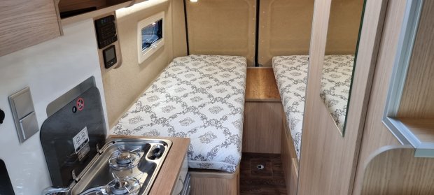 Wnętrze kampera: dwa oddzielne łóżka z wzorzystymi materacami i mała kuchnia.