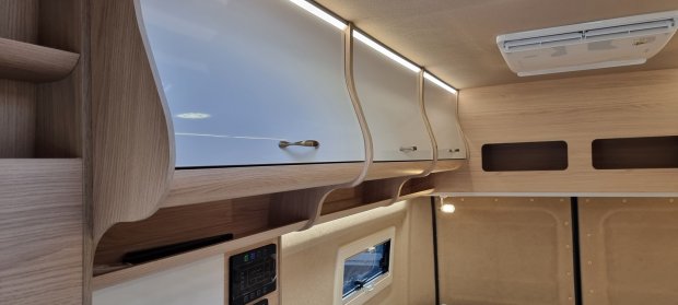 Jasne gięte szafki sufitowe z białymi frontami i LED w kamperze