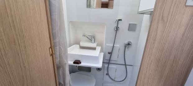 Mała łazienka z umywalką, kranem i prysznicem kabinowym w przestrzeni typu kamper.