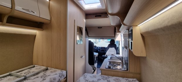 Wnętrze kampera: łóżka, aneks kuchenny i kabina kierowcy.