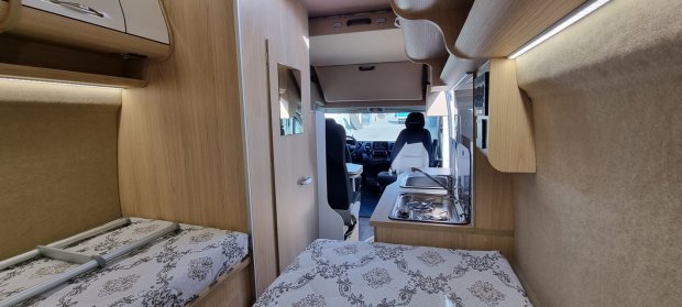 Wnętrze kampera z dwiema kojami, kuchnią i widoczną kabiną kierowcy