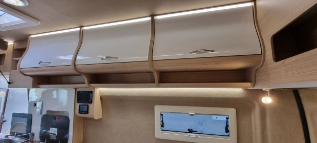 Górne szafki z białymi frontami i LED-owym oświetleniem w wnętrzu kampera