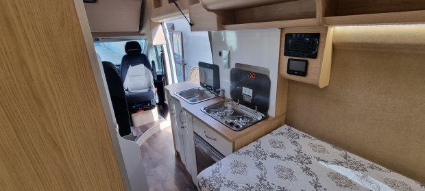 Wnętrze kampera: aneks kuchenny z zlewem, dwupalnikową kuchenką i łóżkiem
