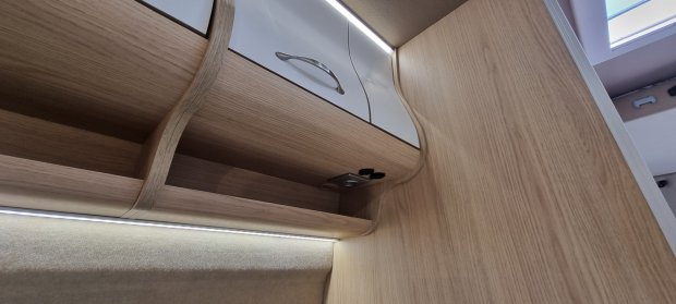 Wnętrze drewnianej szafki z półkami, białymi drzwiczkami, uchwytem i podświetleniem LED.