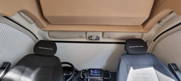 Kabina kampera: dwa fotele z napisem DUCATO, zasłonięta roleta i kokpit