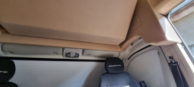 Kabina pojazdu: podniesione beżowe łóżko nad czarnym fotelem z napisem DUCATO