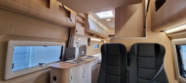 Wnętrze kampera z czarnymi fotelami, kuchenką, zlewem i drewnianymi szafkami.