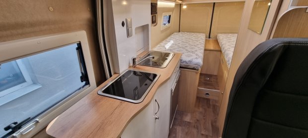 Wnętrze kampera: drewniany blat ze zlewem i płytą grzewczą, dwa pojedyncze łóżka.