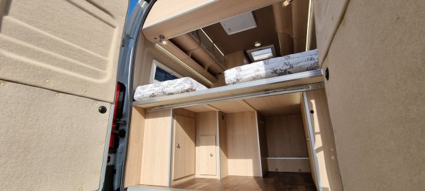 Wnętrze kampera z podwójnym łóżkiem na antresoli i przestronnymi schowkami