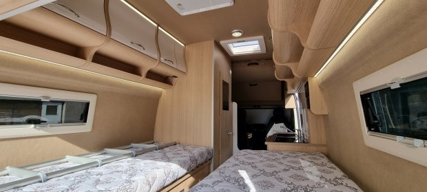 Wnętrze kampera z dwoma łóżkami, drewnianymi szafkami i oknem dachowym